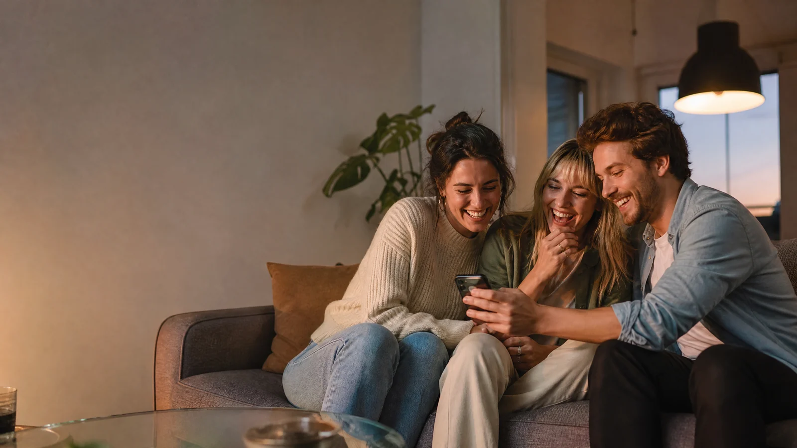 Three fictional adult friends laughing together while viewing a playful photo edit on a phone